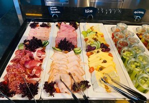 Buffet com diversas opções de comida, incluindo carnes, queijos e frutas.