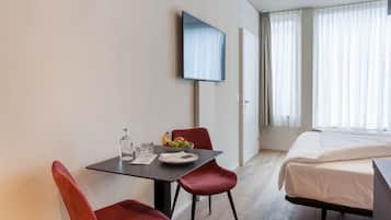 Ett hotellrum med en säng, en tv som är monterad på väggen, ett matbord med stolar och en fruktskål.