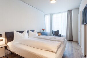 Quarto de hotel com duas camas, uma escrivaninha, uma cadeira e uma televisão.