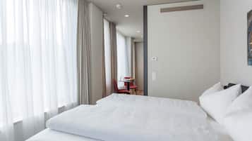 Een hotelkamer met een groot bed, een klein tafeltje met een stoel en een raam met gordijnen.