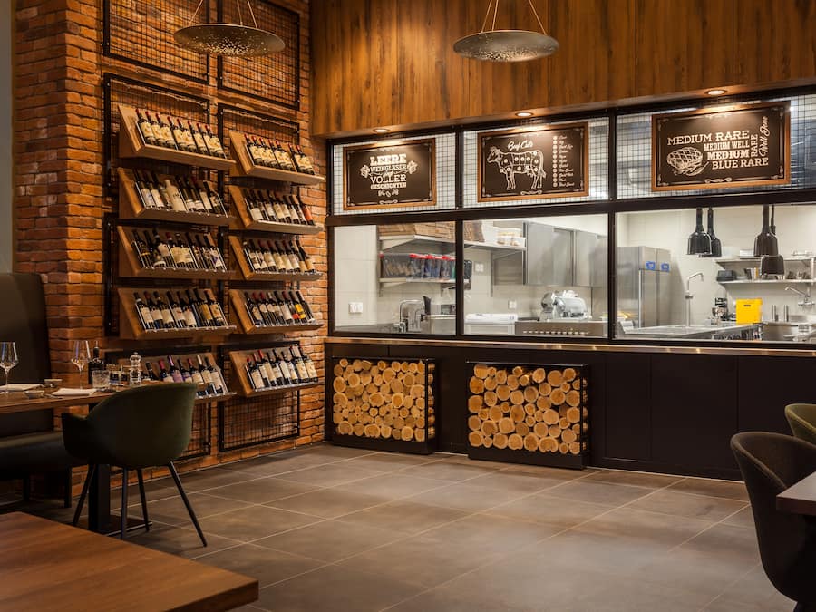 A restaurant interior with wooden walls, wine racks, and a kitchen visible through a glass partition.