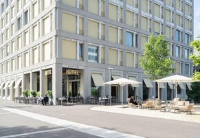 Um hotel com área de estar ao ar livre e um restaurante visível chamado "HIS GRILL & WINE" no andar térreo.