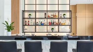 Zona de bar con diseño moderno, que presenta una barra negra y taburetes. Hay varias estanterías con diferentes botellas y copas.