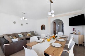 Un salon moderne comprenant un canapé, une table à manger, des chaises et un téléviseur fixé au mur.