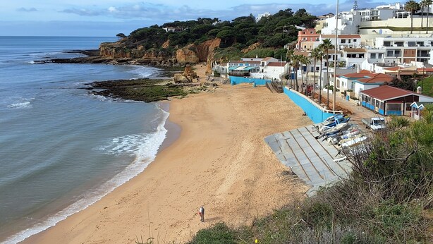 Une plage côtière avec un rivage sablonneux, un promontoire rocheux et une rangée de bâtiments dotés de balcons donnant sur la mer.