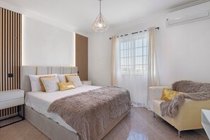 Une chambre à coucher moderne avec un grand lit, une chaise, une table de chevet et un luminaire suspendu.
