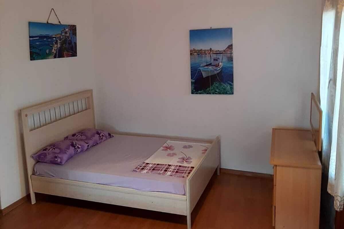 A bedroom with a wooden ceiling, a bed with a headboard, a bedside table, and two wall-mounted pictures.