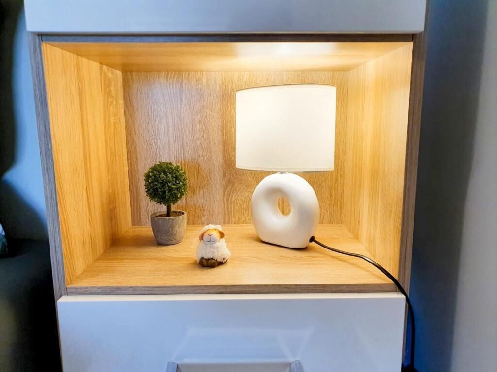 A bedside table with a lamp, a small potted plant, and a figurine.
