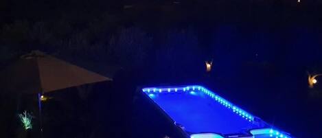 A heated outdoor swimming pool with blue LED lights at dusk.