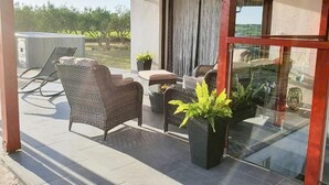 Un patio cubierto con mobiliario de mimbre, plantas en macetas y una puerta de cristal que da a un espacio exterior privado.