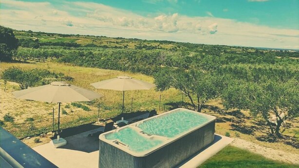 Un jacuzzi con dos sombrillas, rodeado por una zona de piscina con vistas a un paisaje verde.
