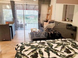 A modern bedroom with a large bed, a sofa, and a balcony with a view.
