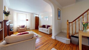 A spacious living room with wooden flooring, a white sofa, a beige sofa, and a wooden staircase. - Princes Street | Oxford Holiday Let | 3 Beds & Sleeps 6 (Oxford)