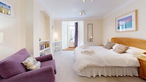 A bedroom with a bed, a purple armchair, a bookshelf, and a large window. - Princes Street | Oxford Holiday Let | 3 Beds & Sleeps 6 (Oxford)