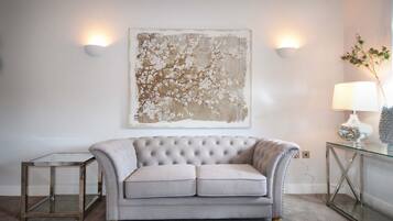 A living room with a tufted grey sofa, a glass coffee table, and a large abstract painting on the wall.