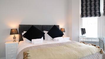 A neatly made bed with a quilted cover, two bedside tables with lamps, and a window with a patterned curtain.