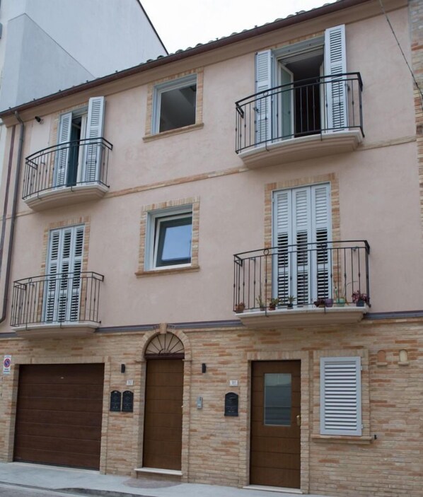Un immeuble à plusieurs étages, doté d’une façade beige, avec une entrée centrale marquée par une porte marron et de nombreux balcons pourvus de garde-corps noirs.