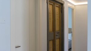 Un couloir avec une porte blanche fermée sur la gauche et une porte à deux vantaux ornée de panneaux décoratifs sur la droite.