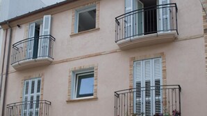 Un bâtiment à deux étages avec une porte marron, une petite fenêtre et un balcon doté d’une rambarde en métal.