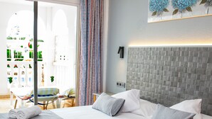 Quarto de hotel moderno com uma cama grande, uma mesinha e vista para o exterior.