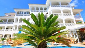 Um hotel com vários andares, varandas, piscina e palmeiras.