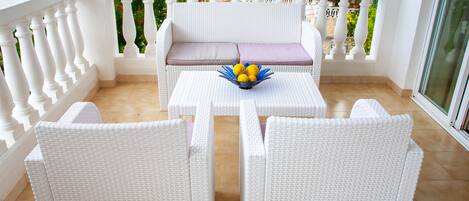 A balcony with white wicker furniture, a cushioned bench, and a table with a bowl of lemons.