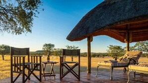 A wooden deck with outdoor furniture, including chairs, a table, and a lounge chair, overlooking a natural landscape. - Ohorongo Tented Camp (Kamanjab)