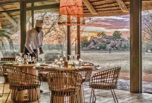 An outdoor dining area with wicker furniture and a view of a natural landscape. - Ohorongo Tented Camp (Kamanjab)