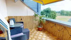 A small balcony with a table and chairs, a potted plant, and a view of the countryside.