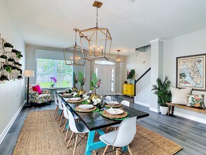 A dining area with a long table, chairs, and a chandelier. - 6BR Villa | Private Pool & Spa, Game Rm, By Disney (Kissimmee)
