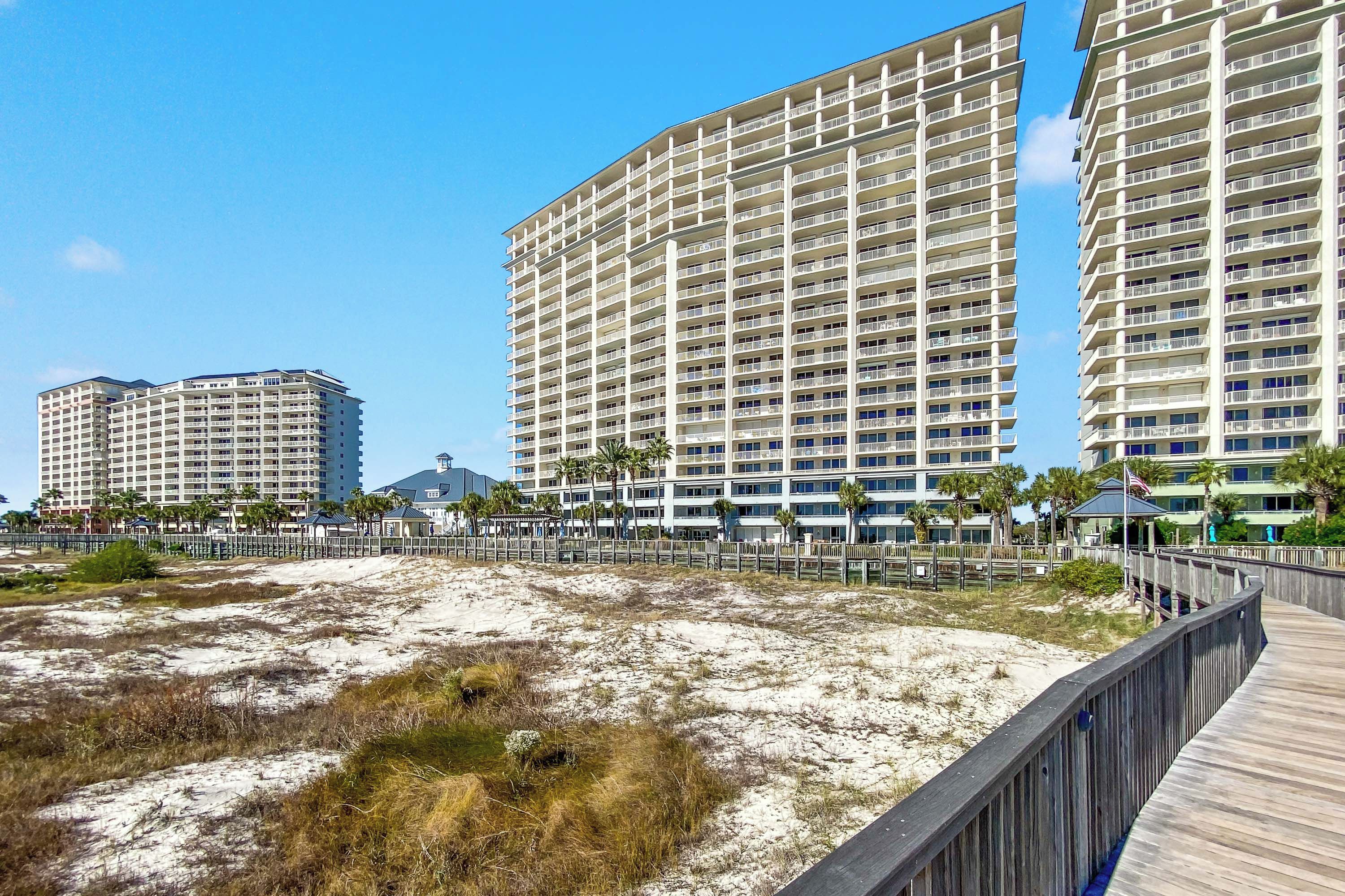 A beachfront hotel with multiple high-rise buildings, a sandy beach area, and a wooden boardwalk.
