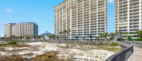 A beachfront hotel with multiple high-rise buildings, a sandy beach area, and a wooden boardwalk.