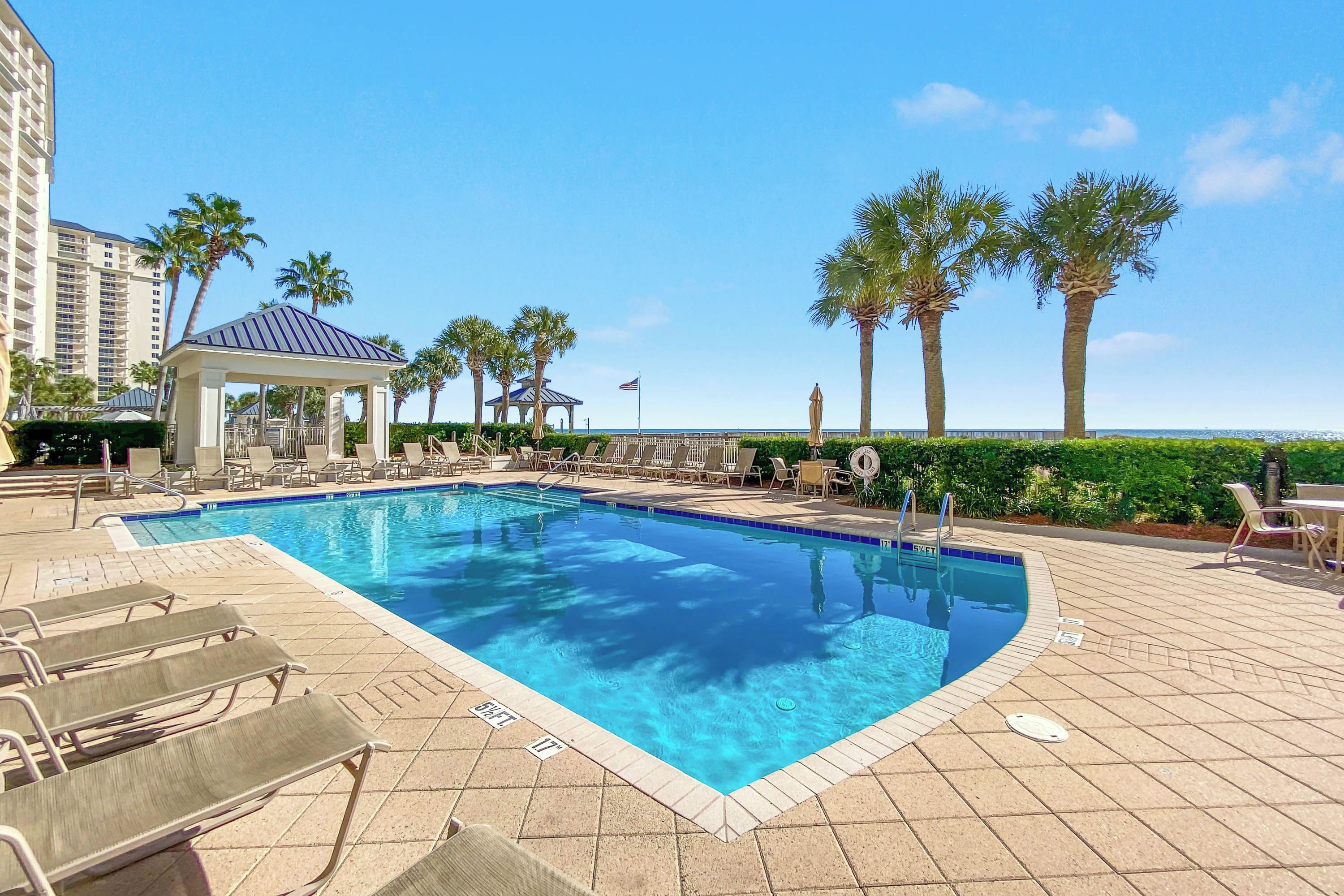 A swimming pool with lounge chairs, palm trees, and a gazebo.
