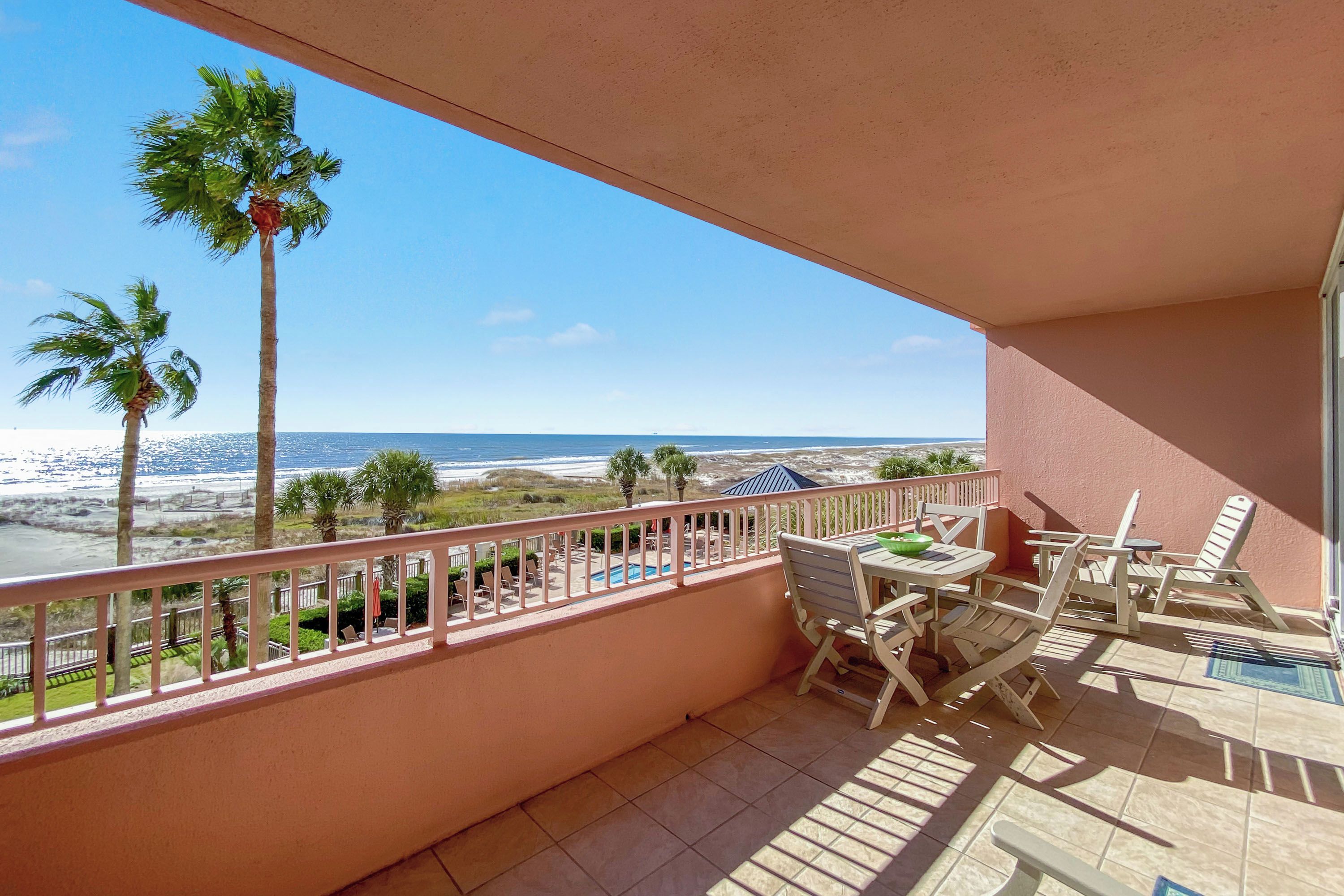 Un balcón con vista a la playa, una piscina y palmeras.