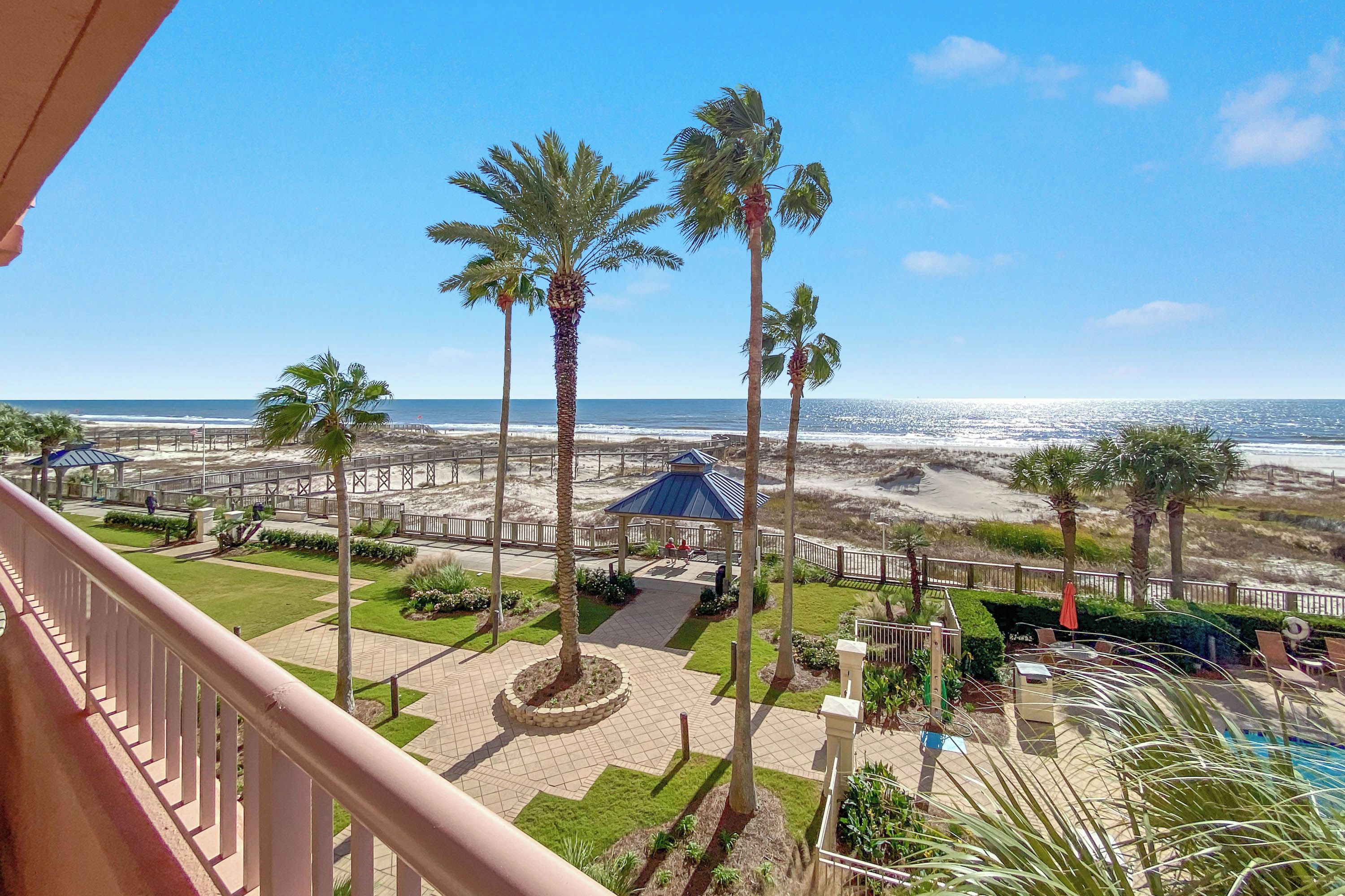 A balcony with a view of a beach, palm trees, and a pool area.