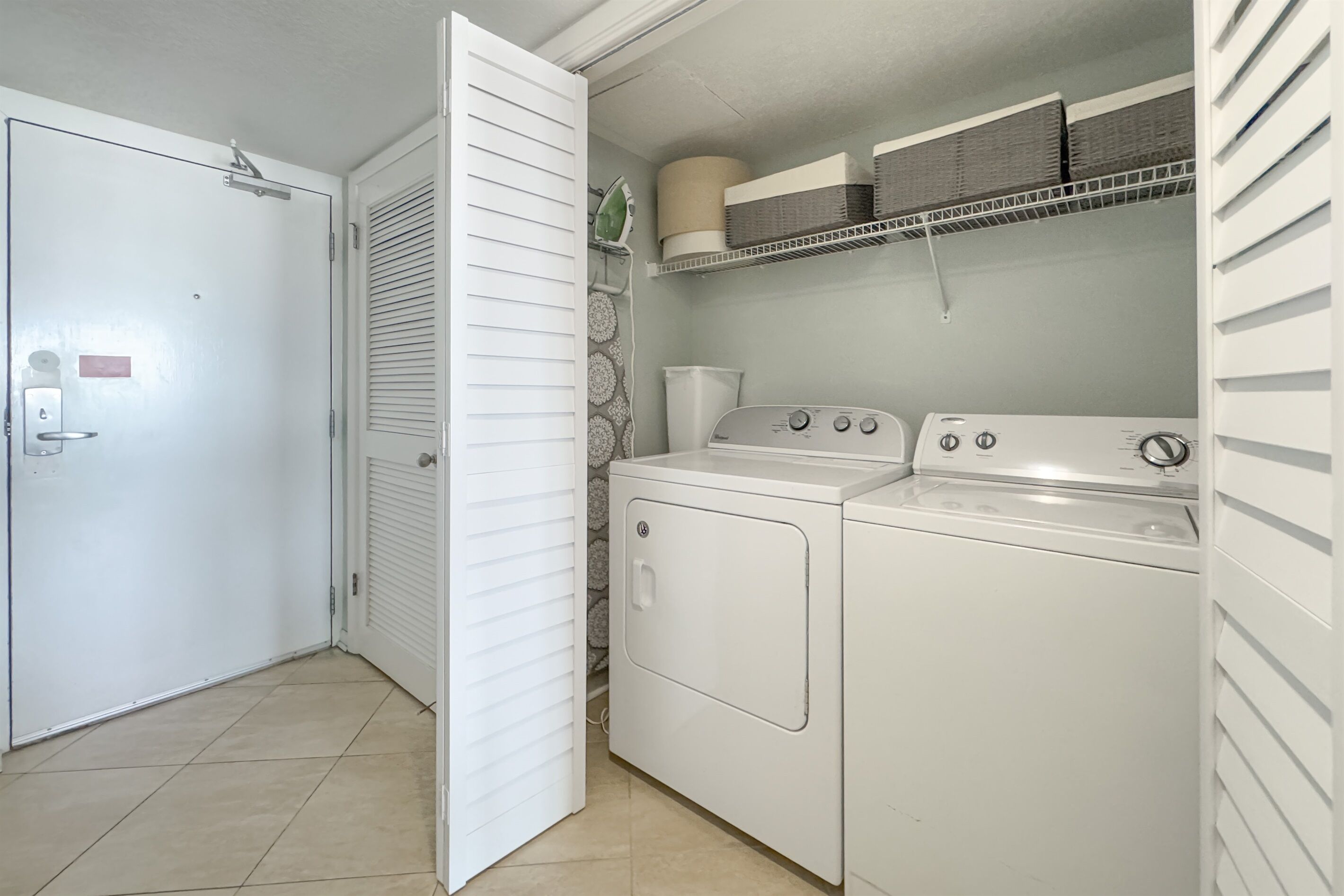 Un espace buanderie comprenant un lave-linge, un sèche-linge et des étagères avec des paniers.