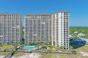 A high-rise hotel with multiple balconies, a swimming pool, and a view of the ocean.