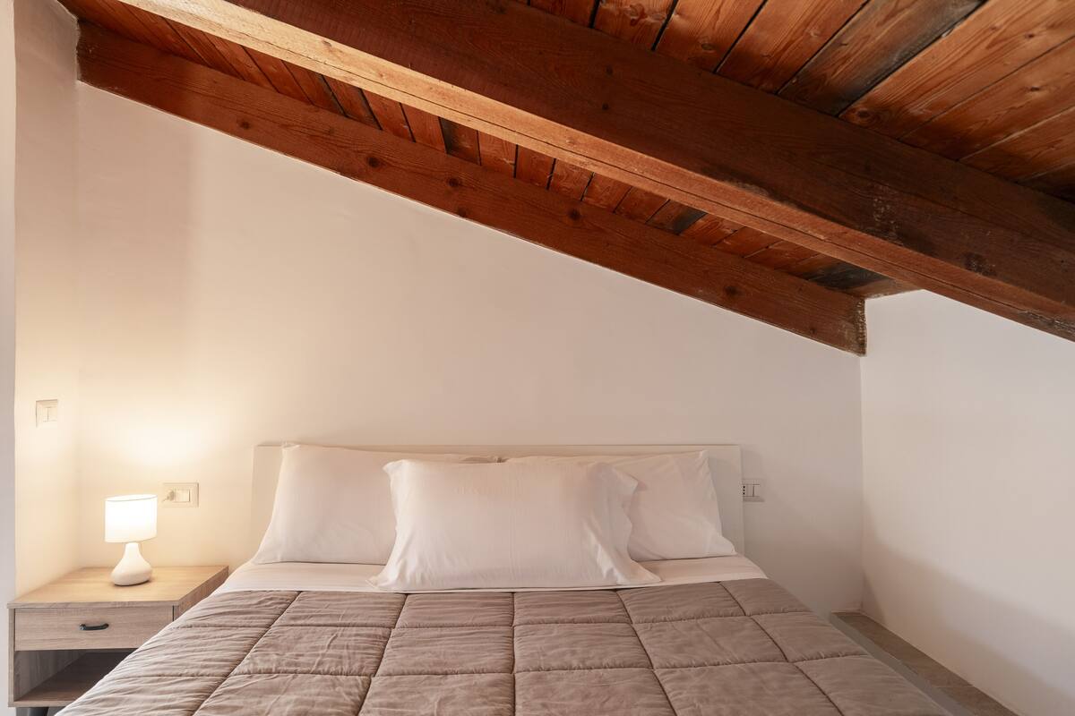 Ein Schlafzimmer mit Holzboden, einem Bett mit weißer Bettwäsche und einem Nachttisch mit Lampe.