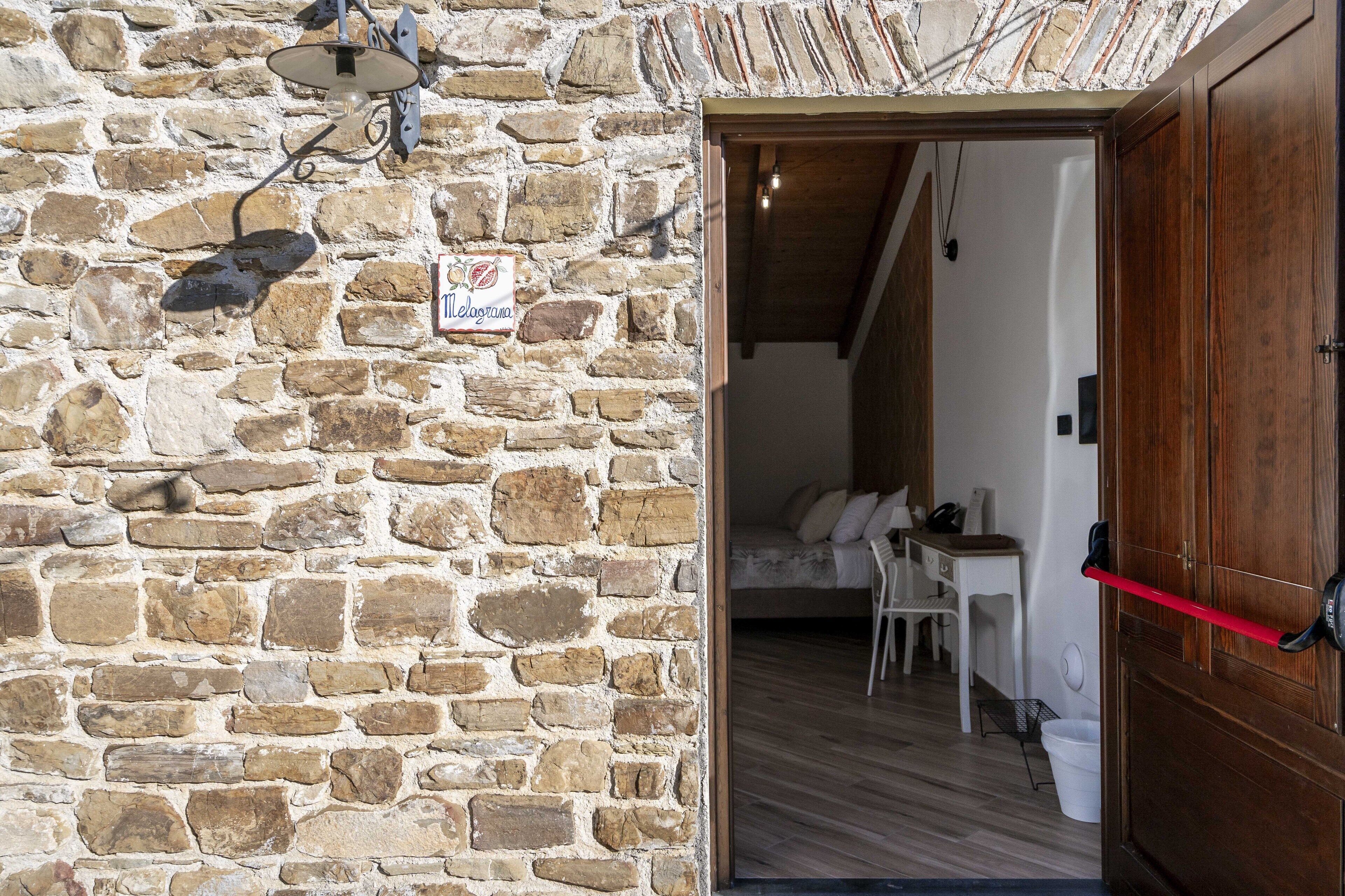 Une pièce avec un mur en pierre sur lequel est accrochée une pancarte, une porte en bois, un lit, un bureau et une chaise.