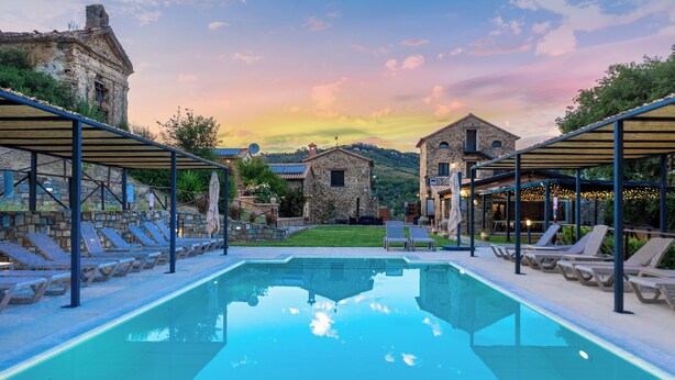 A swimming pool with lounge chairs, stone buildings, and a sunset sky. - Le Querce Farmhouse (Agropoli)