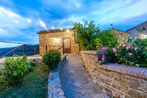 A stone building with a wooden door, a stone pathway, and a brick wall with flowers. - Le Querce Farmhouse (Agropoli)