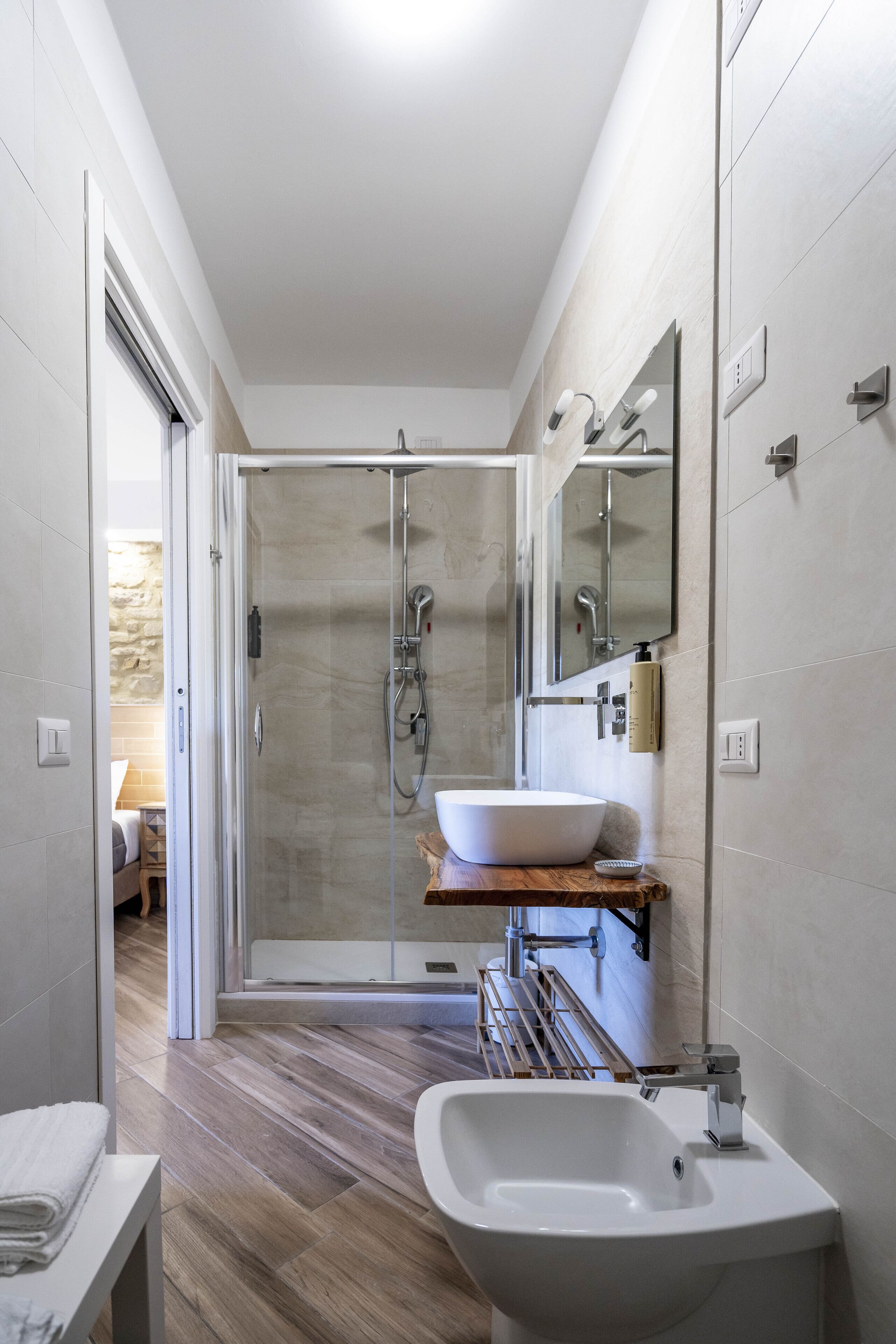 A modern bathroom with a glass-enclosed shower, a white sink, and a wooden shelf.