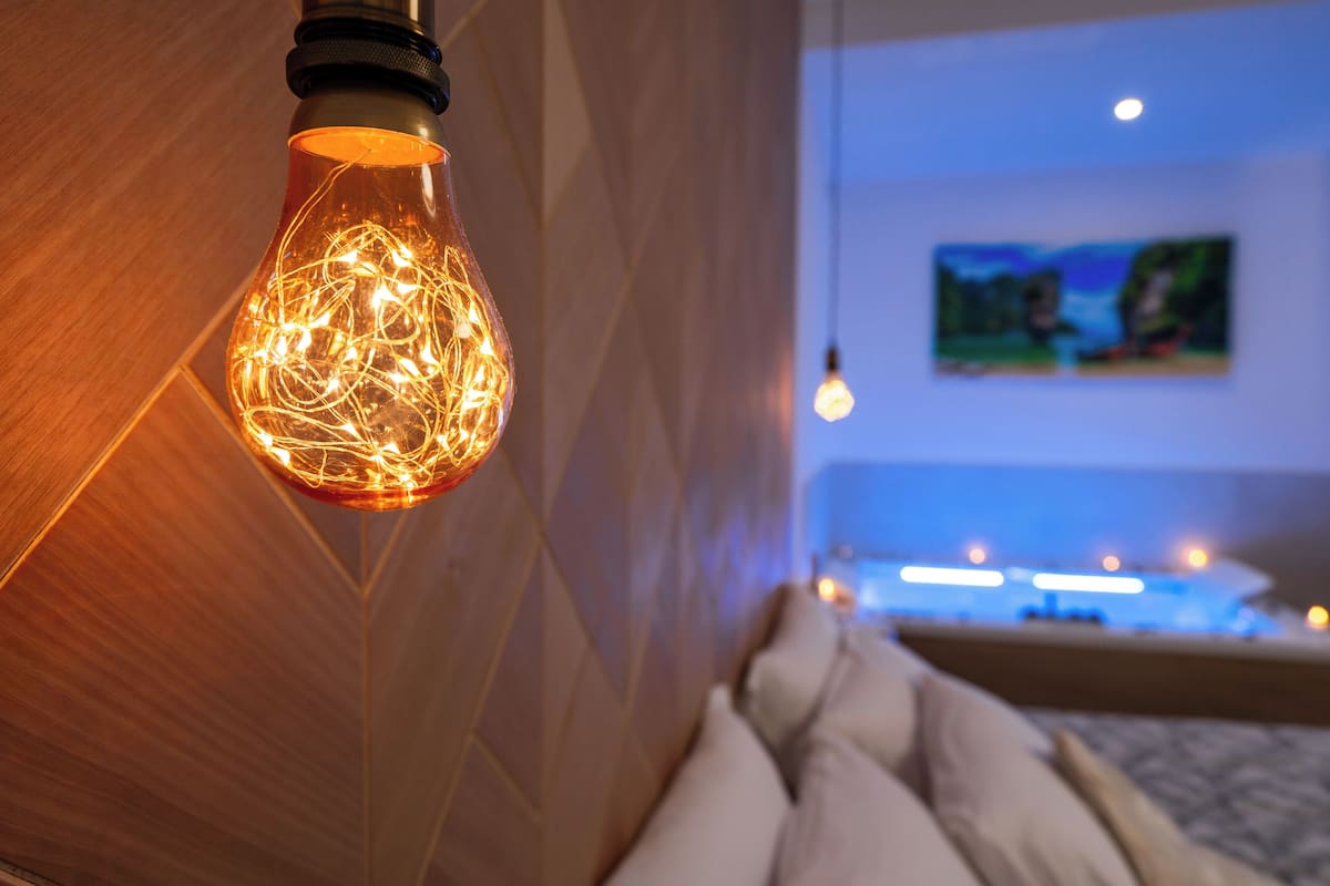 Ein modernes Hotelzimmer mit einer besonderen Leuchte, einem Gemälde an der Wand und einem Bett mit weißem Kopfteil.