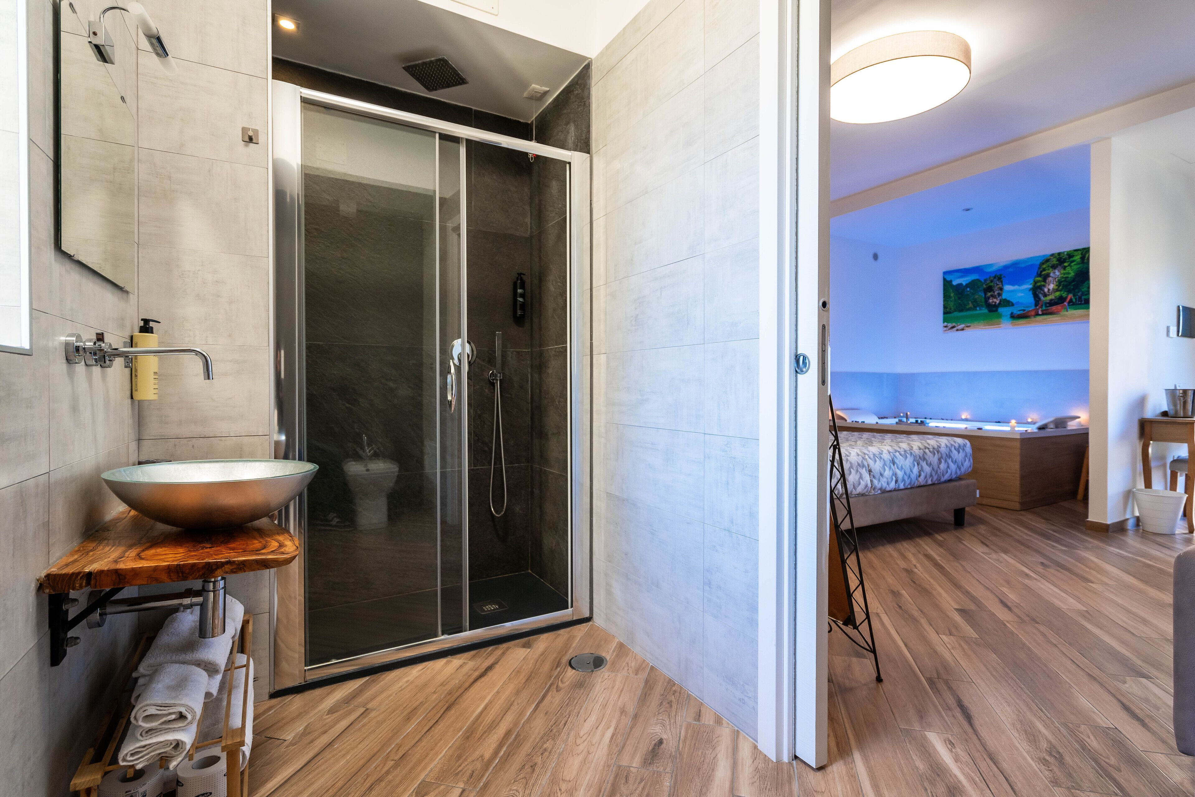 A modern bathroom with a glass shower enclosure, a wooden vanity with a large sink, and a wooden floor.