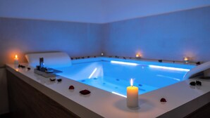 A modern spa room with a heated pool, a white bathtub, and a lit candle on the edge. - Le Querce Farmhouse (Agropoli)