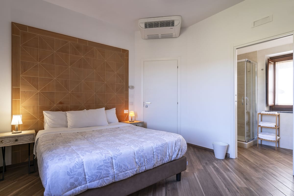 Ein Schlafzimmer mit einem großen Bett, einem Holzkopfende, Nachttischlampen, einer weißen Tür und einer Duschkabine.