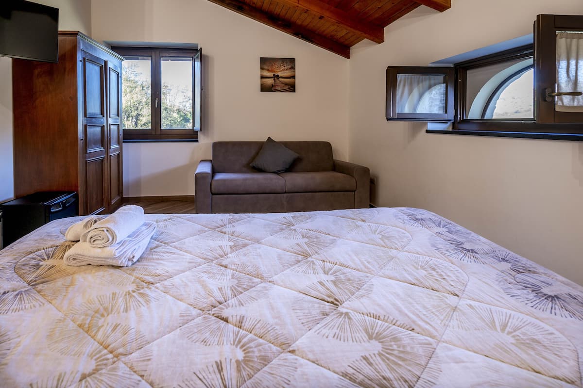 Ein Schlafzimmer mit einem Bett, einer Couch, einem Fenster und einem Bild an der Wand.