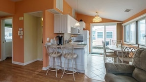 Una cocina compacta con armarios blancos, una isla central con taburetes y un comedor con mesa y sillas.