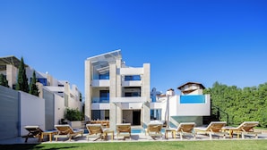 Un hotel moderno de varios pisos con zona de piscina, tumbonas y un cielo azul despejado.