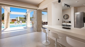 Una cocina moderna con una isla grande, horno empotrado y refrigerador. Se ve una piscina a través de las puertas corredizas al patio.
